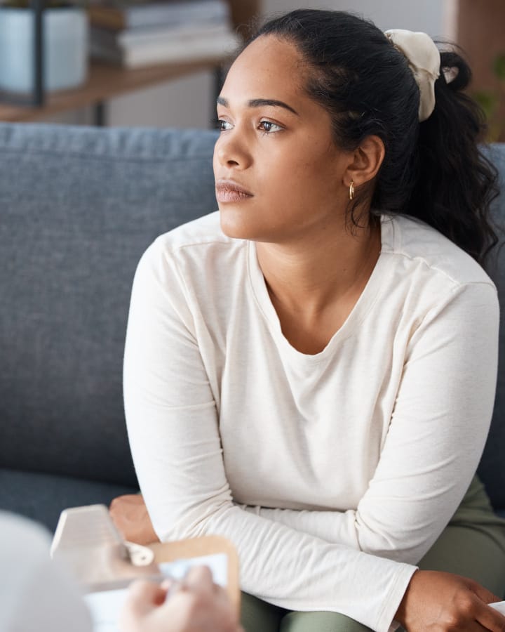 A young female sitting and looking off into the distance, as a doctors clipboard can be seen in the corner of the shot performing some kind of patient intake.